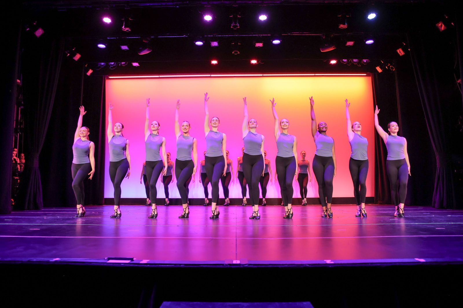 PDC dancers on stage in unison with arms raised during the Performance Collective live performance
